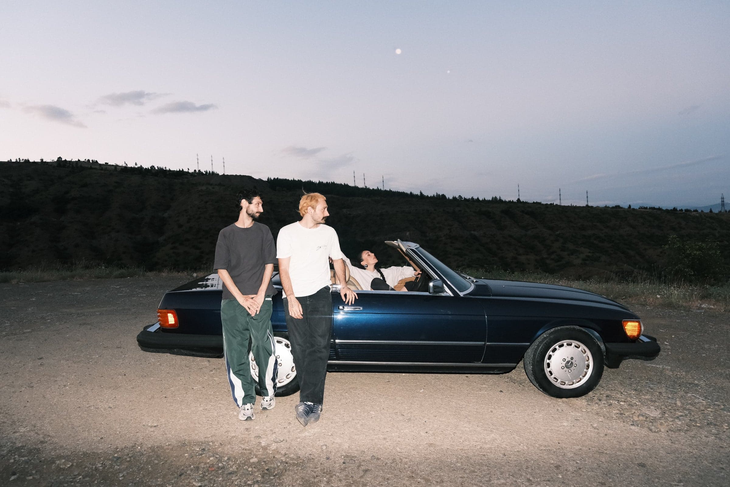 Three people with a dark blue convertible at dusk