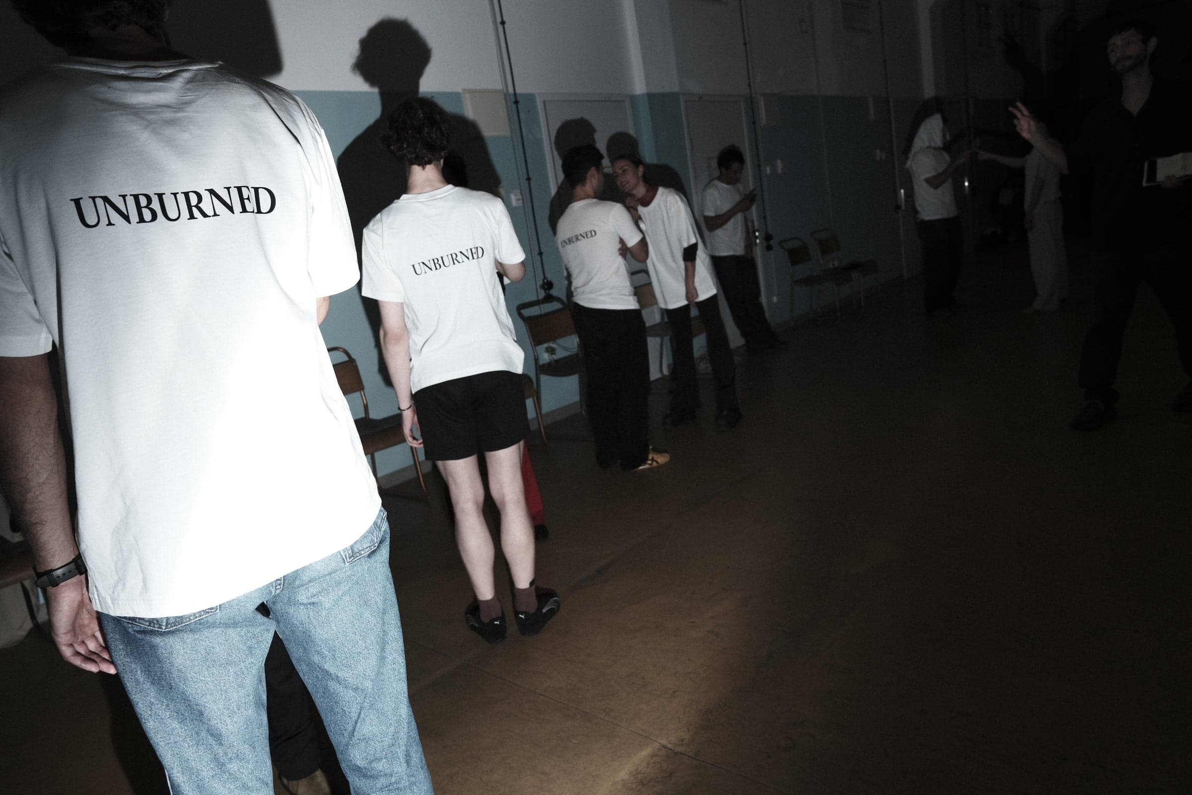 Performers in white UNBURNED T-shirts backstage