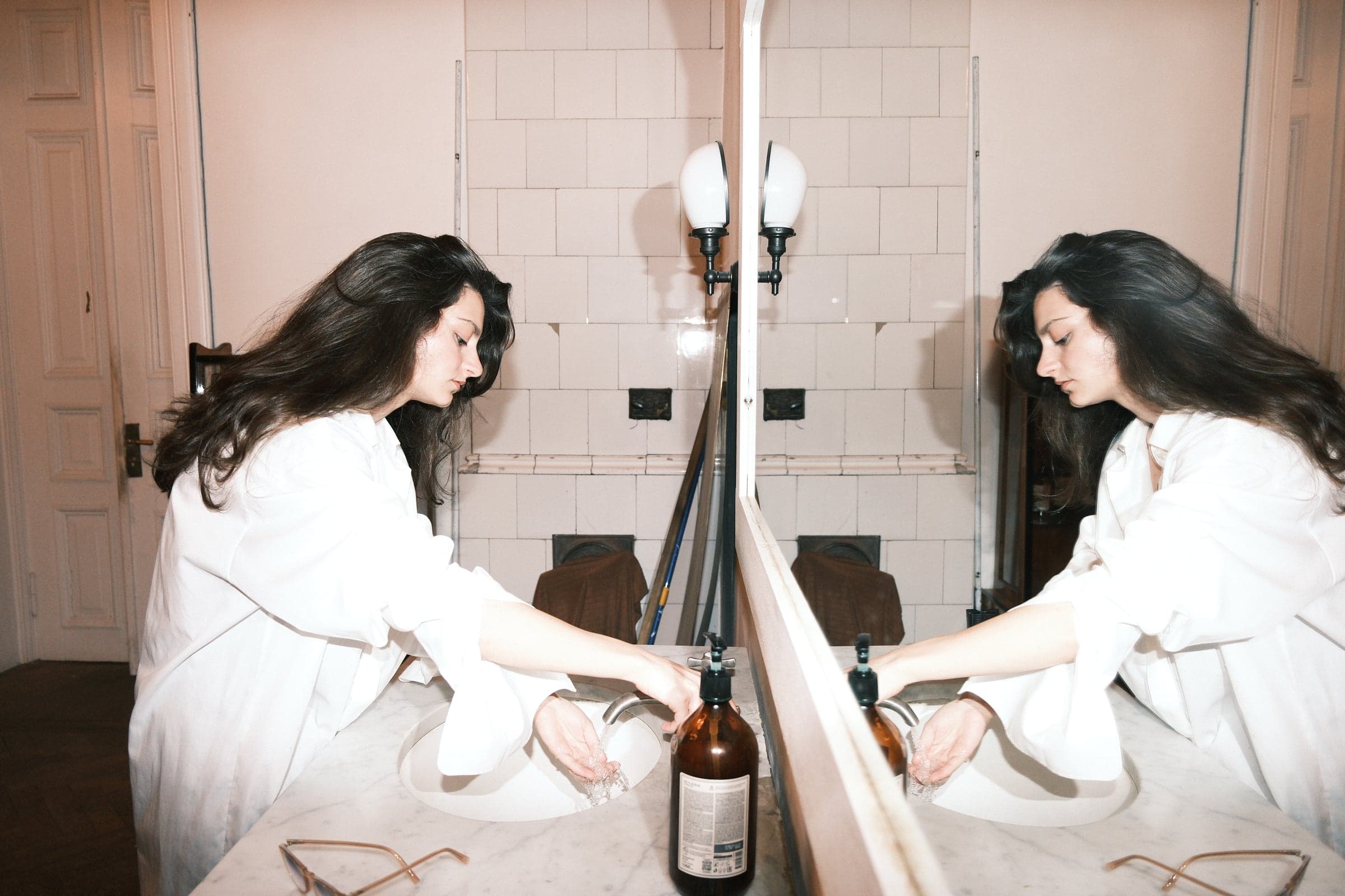 A performer in white reflected in a bathroom mirror